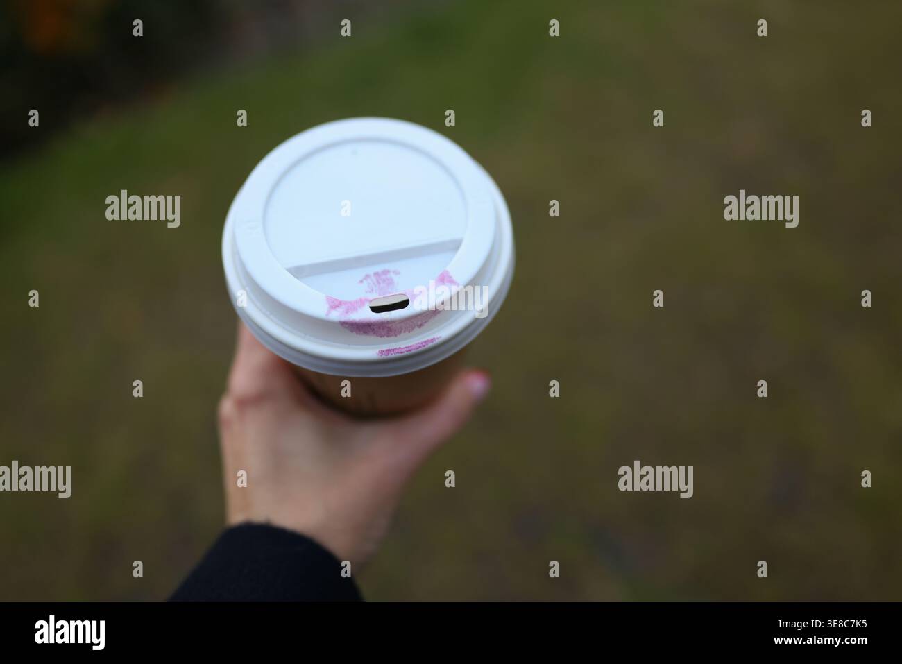 Main tenant une tasse à café à emporter avec marque de rouge à lèvres, détail style de vie urbain et concept de routine matinale. Banque D'Images
