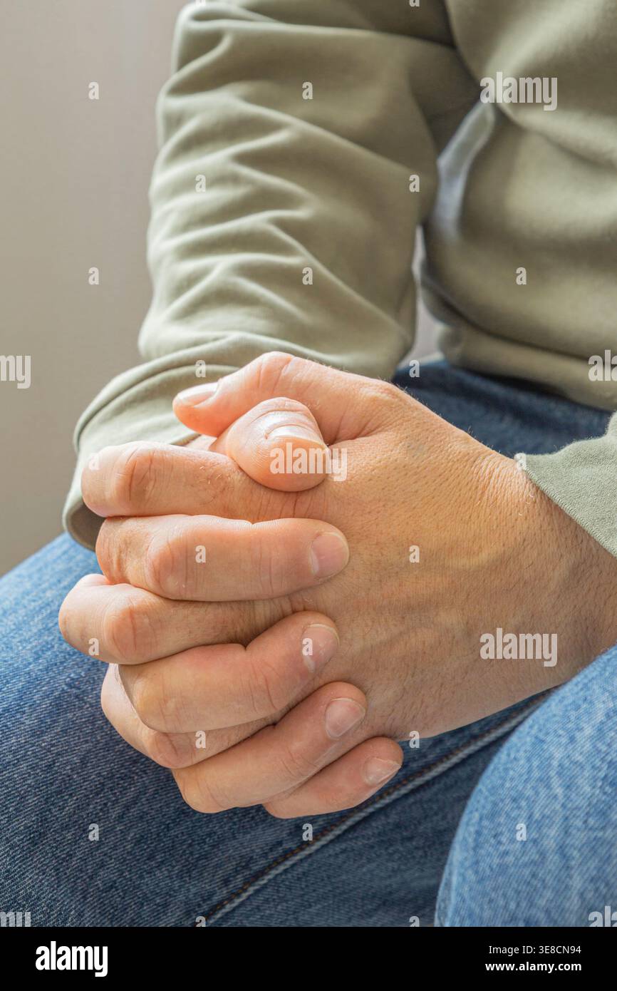Gros plan de mains serrées se reposant ensemble, symbolisant la contemplation, la patience ou un reflet tranquille dans un cadre intérieur calme et baigné de lumière naturelle douce. Banque D'Images