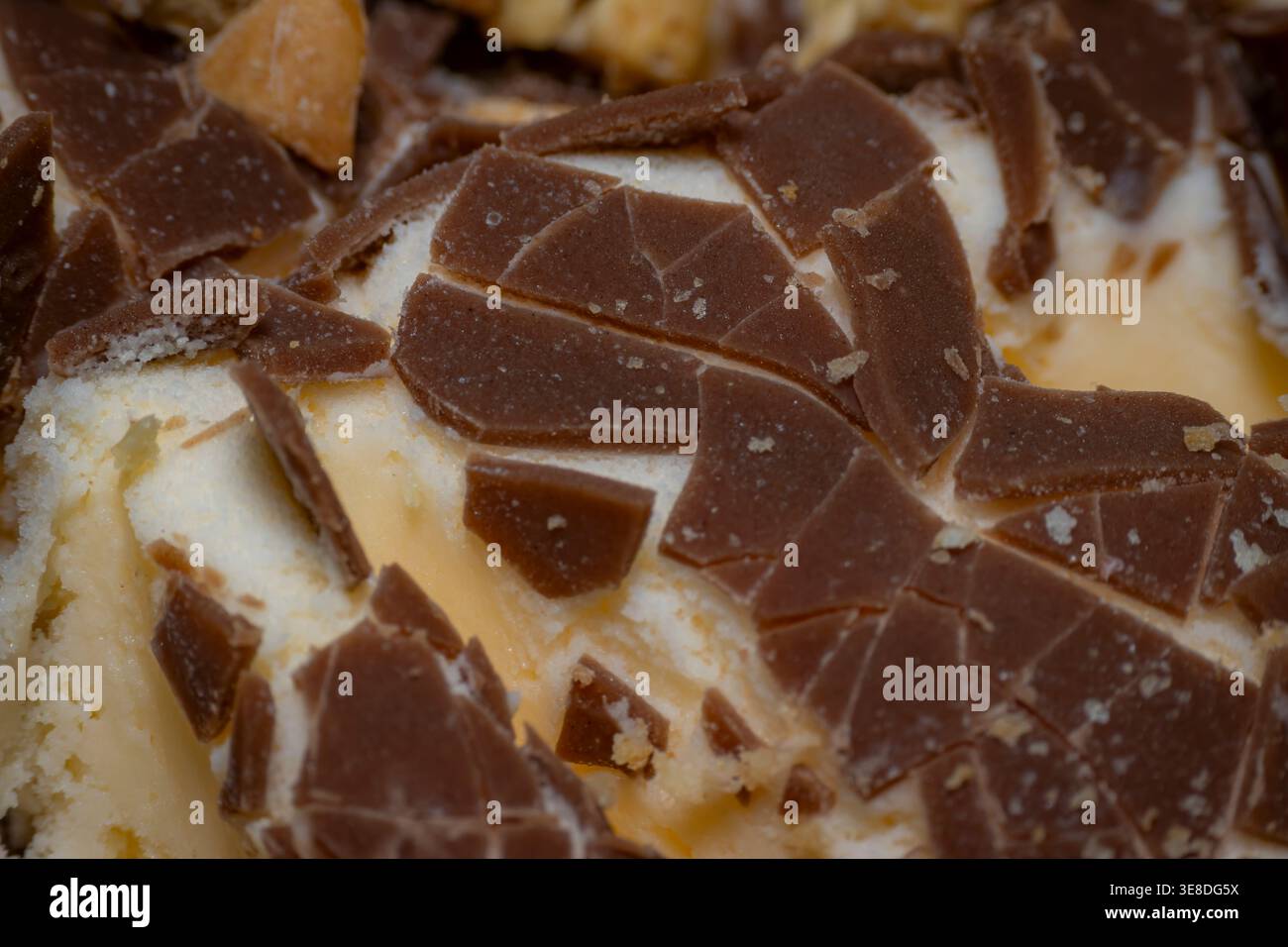 Détail gros plan de morceaux de chocolat au lait fragmentés incorporés dans une crème glacée molle à la vanille sur un dessert, montrant la texture et les détails du cacao Banque D'Images