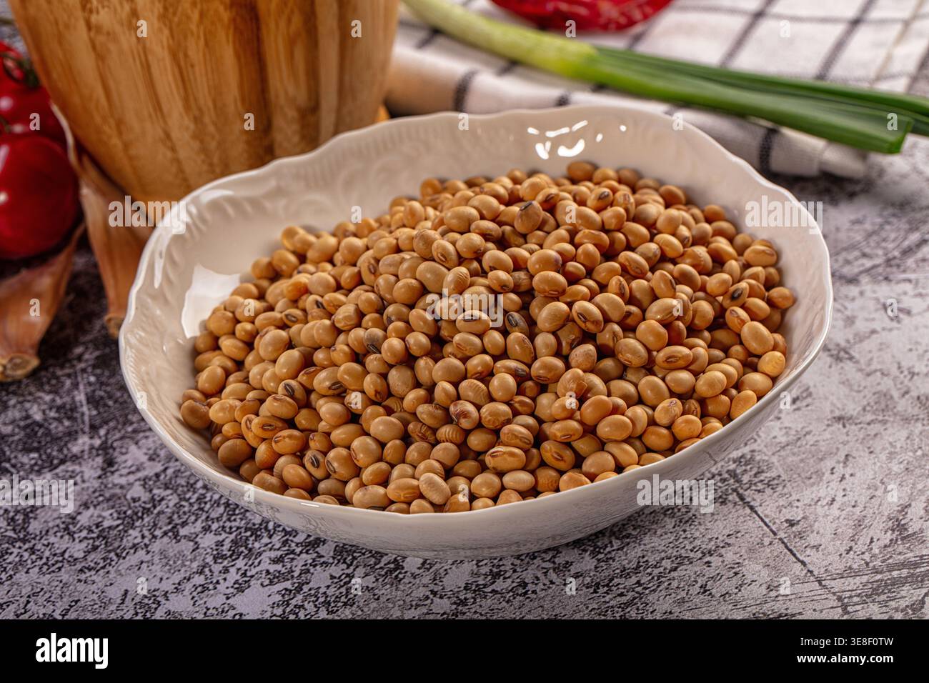 Bol blanc débordant de soja cru, un ingrédient essentiel pour une cuisine saine. La lumière naturelle met en valeur les tons terreux des grains de café. L'arrière-plan montre f Banque D'Images