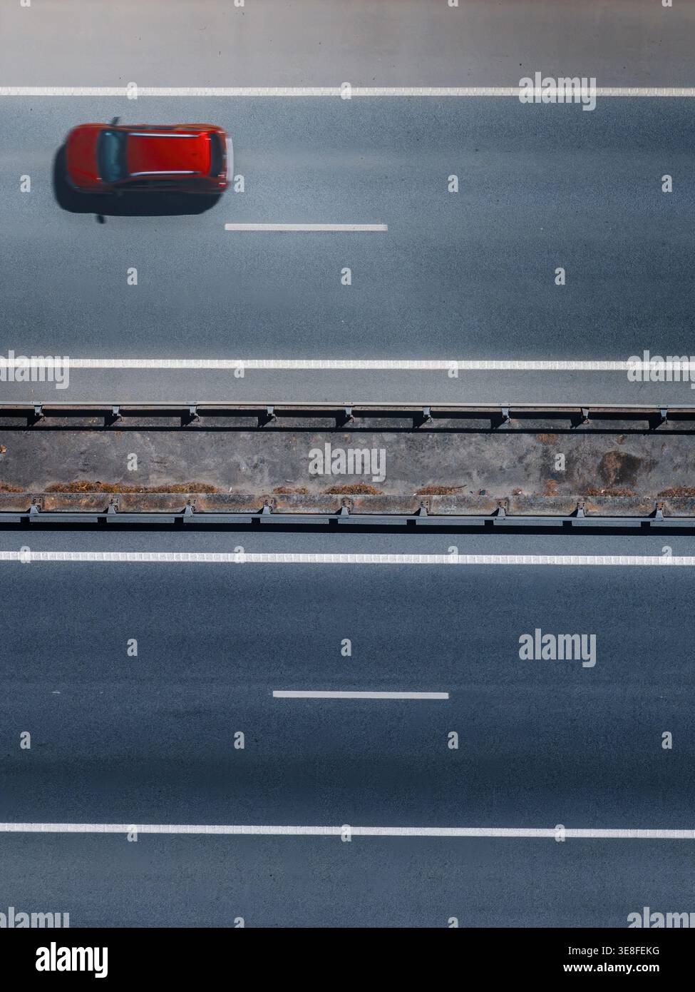 Vue aérienne d'une seule voiture rouge circulant le long d'une autoroute asphaltée moderne avec des marquages de voie blancs et une barrière de sécurité centrale à Cascais. Banque D'Images