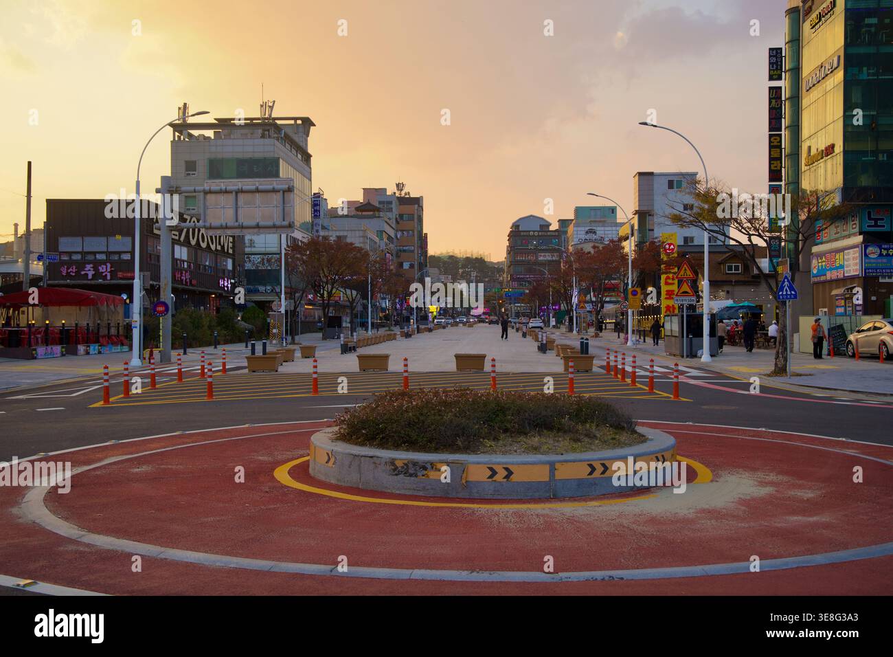 La route de la plage d’Ilsan Beach part d’un petit rond-point, bordée de boutiques, d’arbres d’automne et de lumière du soir dans le quartier de Dong-gu à Ulsan. Banque D'Images