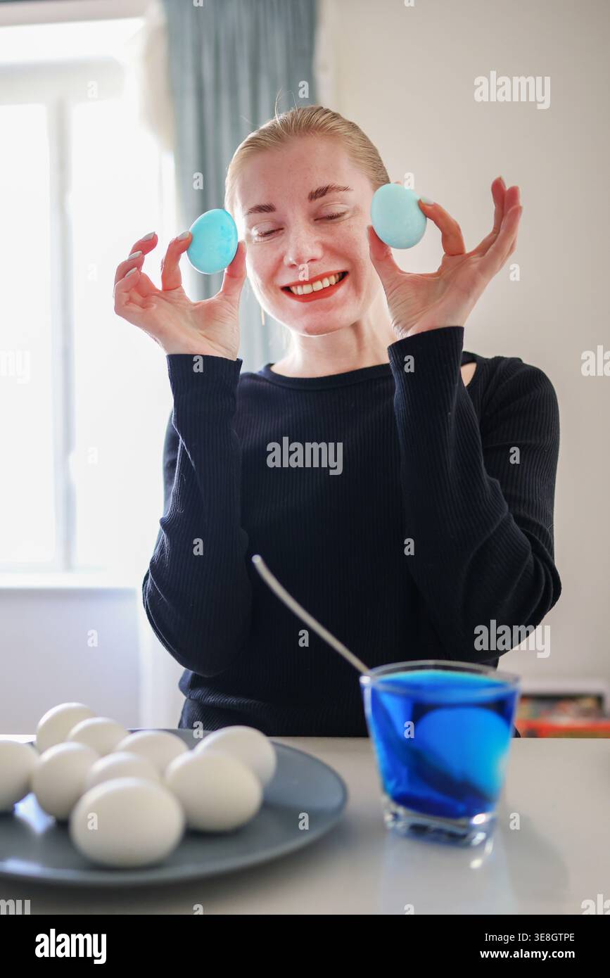 Femme tenant des œufs de Pâques bleus au-dessus des yeux, humeur ludique et célébration festive du printemps. Banque D'Images