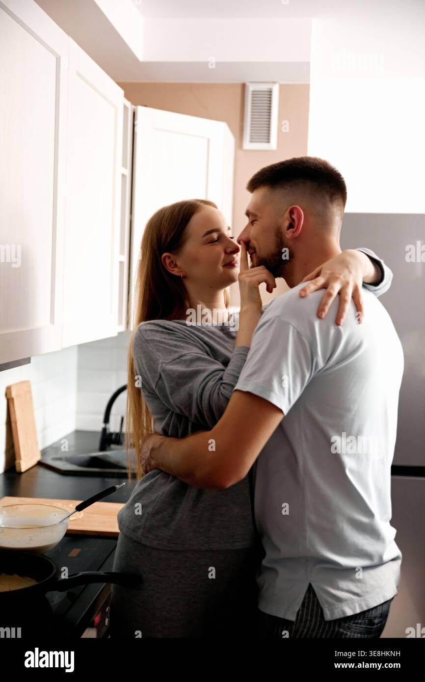 Un couple profite d'un moment proche dans la cuisine. Ils préparent la nourriture ensemble tout en souriant et en s’engageant les uns avec les autres. Le réglage est lumineux et Banque D'Images