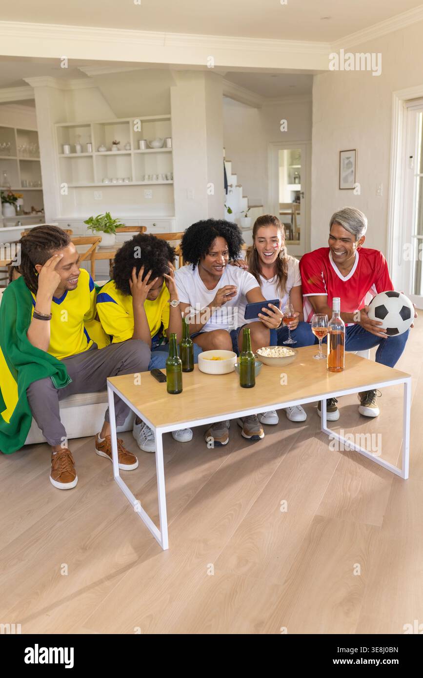 Divers amis portant des maillots de football regarder le match sur le téléphone à la maison avec des bières de football Banque D'Images