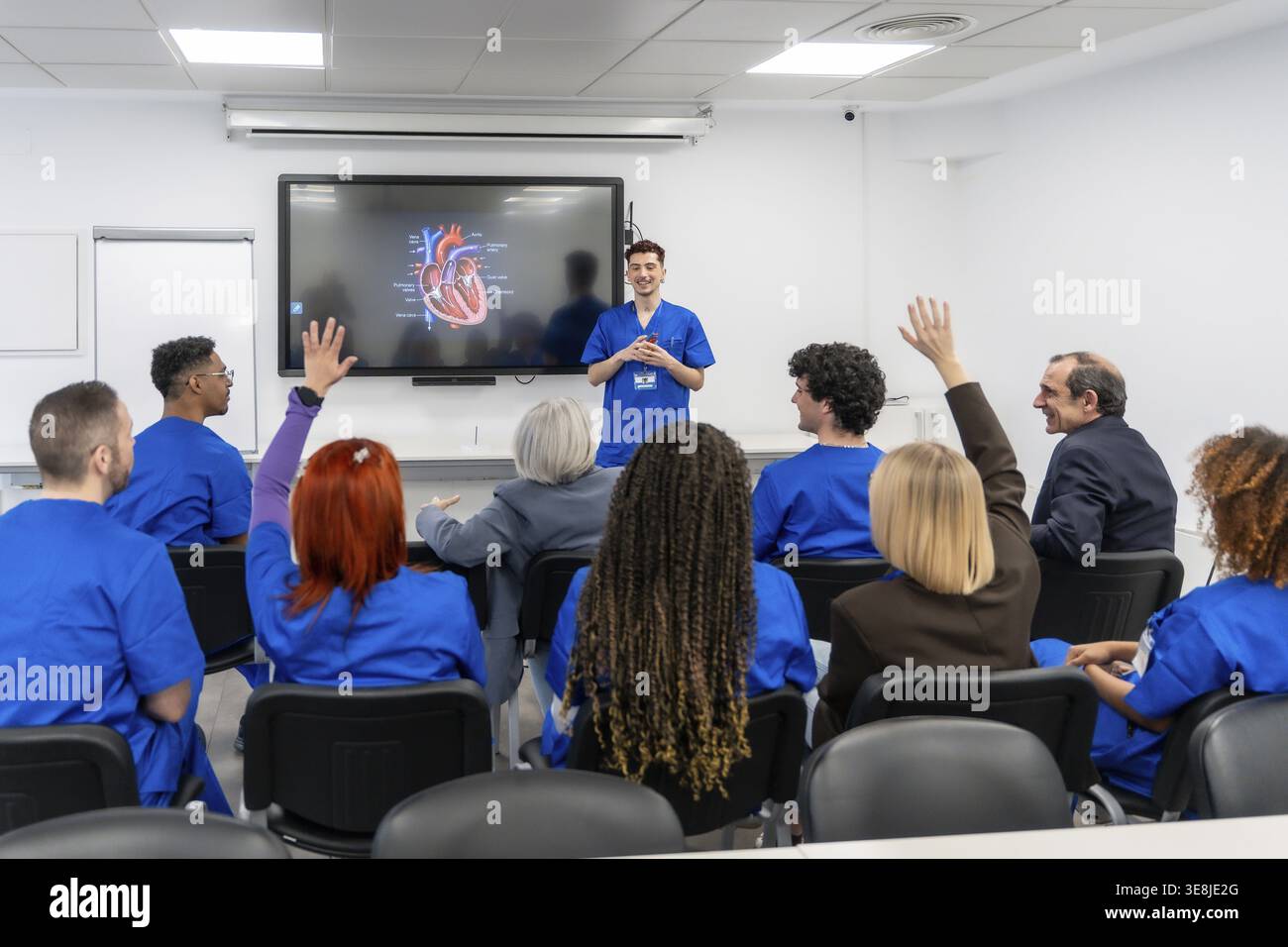 Un groupe diversifié d'étudiants et de professionnels de la santé participent activement à un séminaire de formation médicale, levant la main pour poser des questions lors d'une pré Banque D'Images