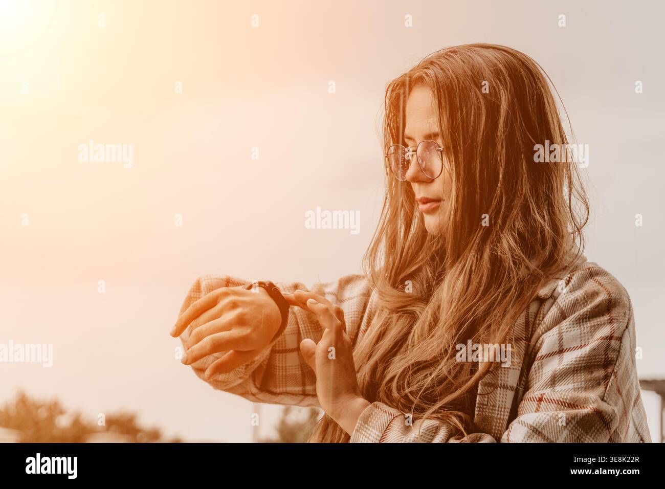 Smartwatch femme vérifiant jeune femme dans des lunettes regardant sa montre intelligente à l'extérieur au coucher du soleil avec beaucoup d'espace de copie Banque D'Images