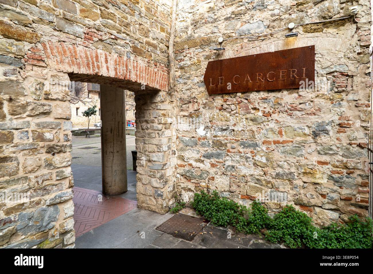 Une arche en pierre altérée mène à une pittoresque cour européenne avec un panneau rustique au-dessus Banque D'Images
