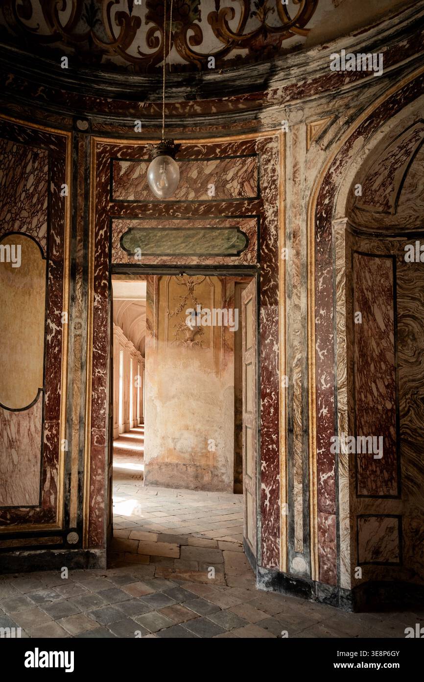 AGLIÈ, ITALIE – OCTOBRE 2025 : vue intérieure du château d'Agliè montrant des murs peints ornés, des textures de marbre vieilli et des portes menant à un corrido ensoleillé Banque D'Images