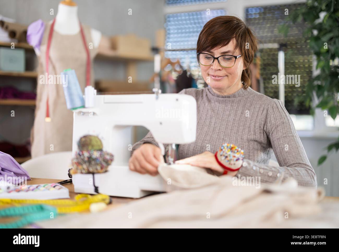 Travailler dans un atelier de couture - couturière femme travaillant à la machine à coudre faisant des points sur le tissu Banque D'Images