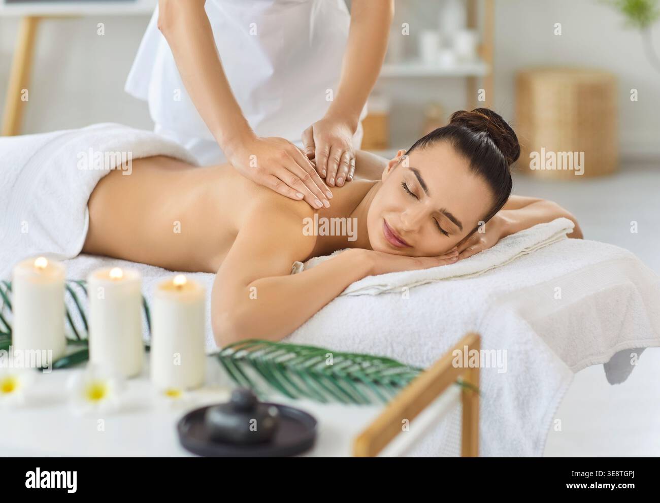 Femme souriante allongée sur la table de massage, appréciant le soin relaxant du dos et des épaules dans le salon de spa. Banque D'Images