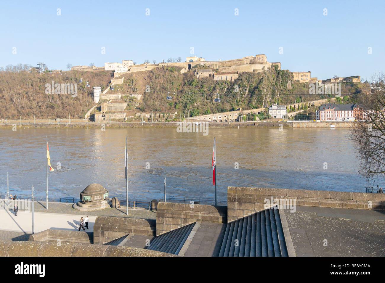 Coblence, Allemagne - 02.26.2026 : vue de Deutsches Eck in Coblence à la forteresse d'Ehrenbreitstein et au Rhin avec drapeaux ciel bleu ensoleillé Banque D'Images