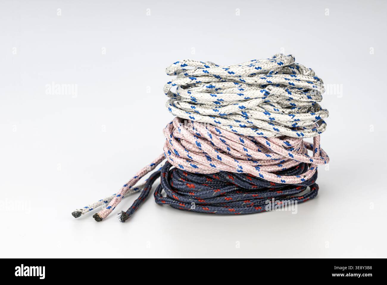 Photographie de produit professionnel de cordes tressées enroulées avec des couleurs blanc crème, rose poussiéreux et bleu marine avec des motifs de diamant contrastés stac Banque D'Images