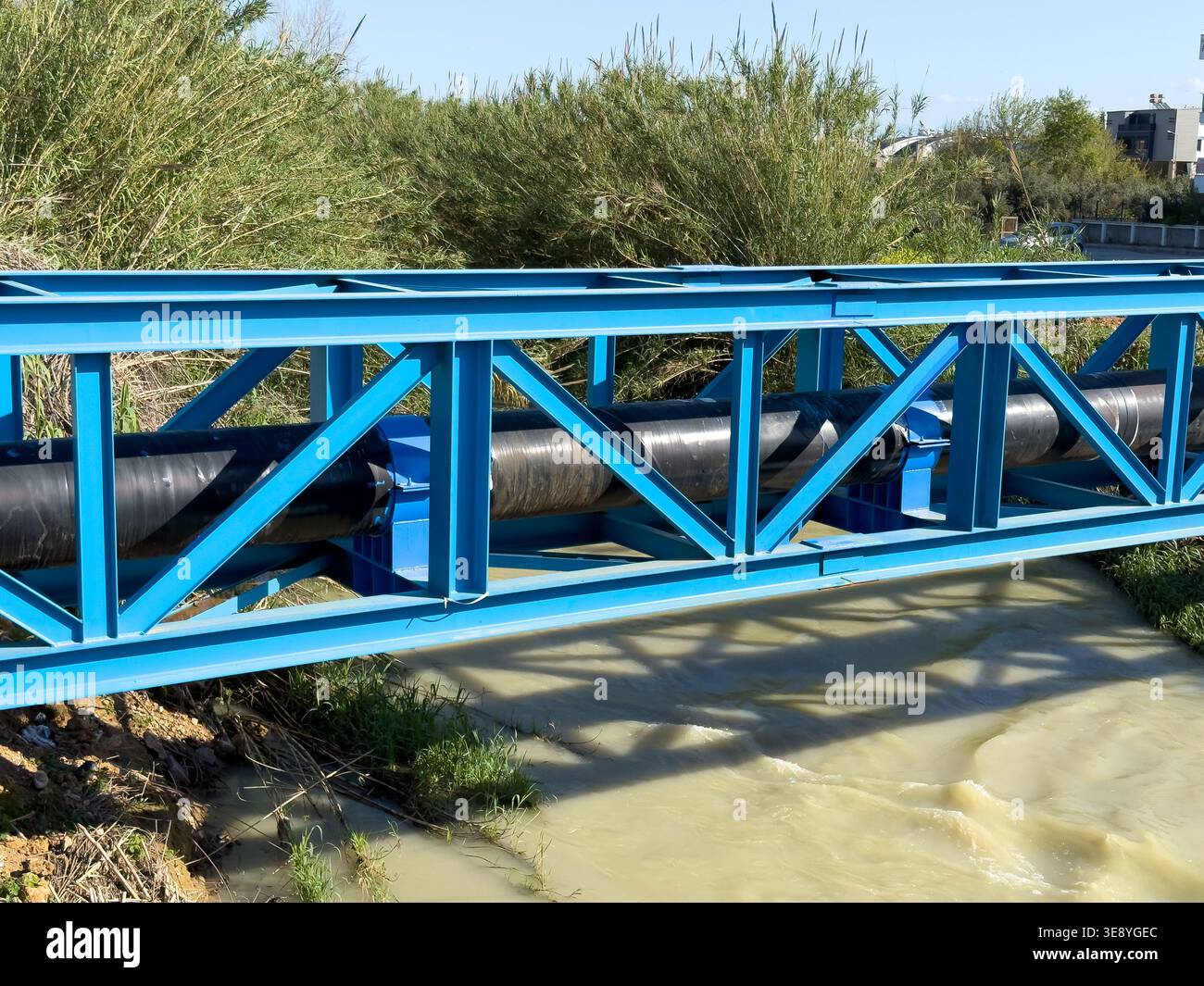 Pont en treillis d'acier bleu soutenant un grand pipeline industriel au-dessus d'une rivière qui coule Banque D'Images