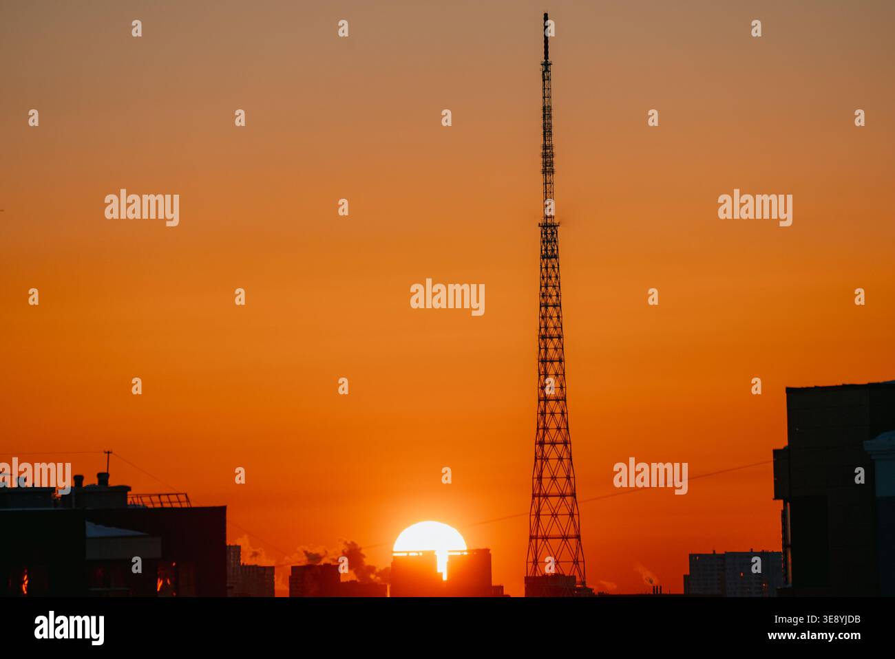 Silhouette de tour de radio s'élevant au-dessus des bâtiments de la ville au coucher du soleil, avec un ciel orange et jaune vibrant formant une toile de fond colorée, représentant la vie urbaine moderne et la connectivité technologique Banque D'Images