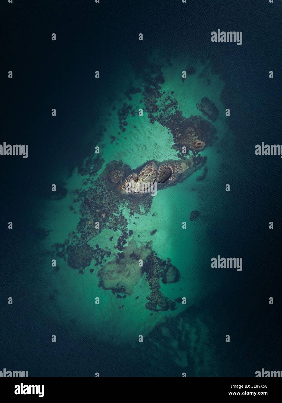 Vue aérienne de l'affleurement rocheux de Sakrisoya entouré d'une eau turquoise vibrante peu profonde et d'une mer profonde sombre à Moskenes, Nordland, Norvège. Banque D'Images