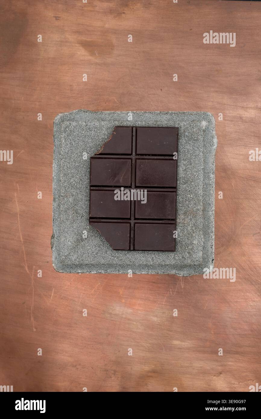 Composition minimaliste avec une mini barre de chocolat mordue sur des textures de ciment et de cuivre. Banque D'Images