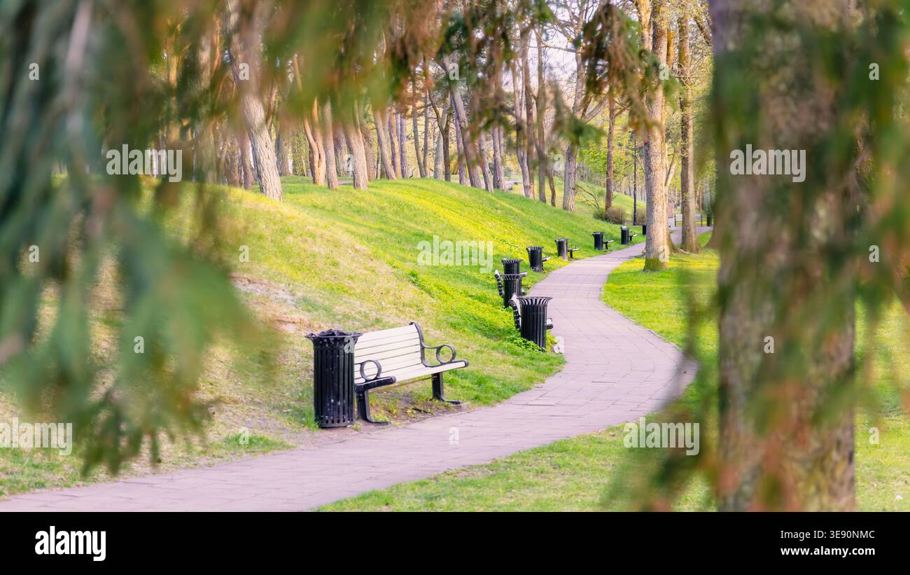 Mouvement doux à travers l'espace dans le sentier sinueux avec des bancs et des pentes vertes dans le parc Liepaja, la lumière du printemps tôt crée une direction calme et l'urb ouvert Banque D'Images