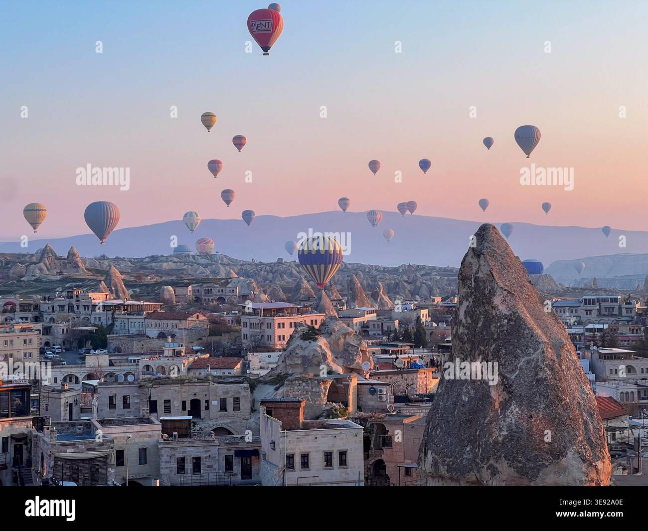 Montgolfières volant au-dessus des cheminées de fées et des maisons de grottes au coucher du soleil, Goreme, Cappadoce, Turquie - Image de stock capturée avec un smartphone