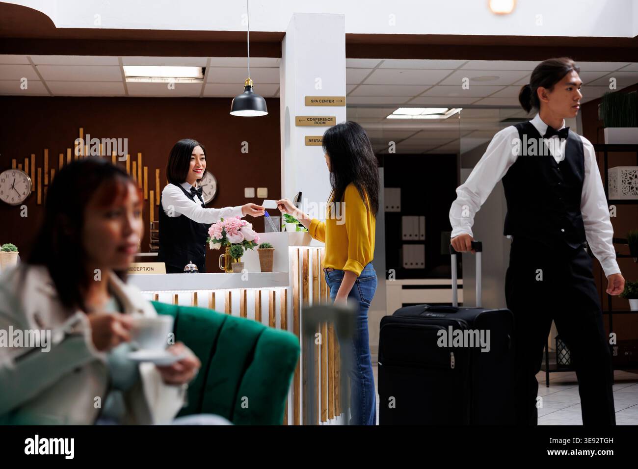 Le visiteur reçoit une carte-clé de la réceptionniste asiatique dans le hall contemporain de l'hôtel et est ensuite présenté à la chambre. Le voyageur est assisté par un personnel amical à l'arrivée dans le complexe moderne Banque D'Images