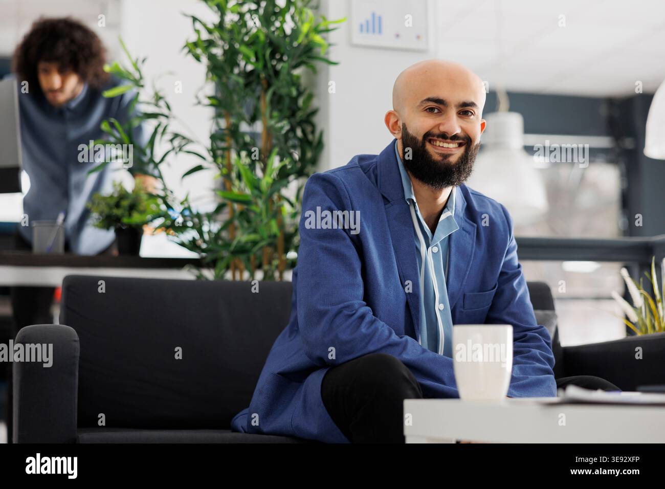 Entrepreneur d'affaires arabe souriant regardant la caméra tout en étant assis sur le canapé dans le bureau. Start-up manager exécutif à succès portant un portrait de costume dans l'espace de coworking Banque D'Images