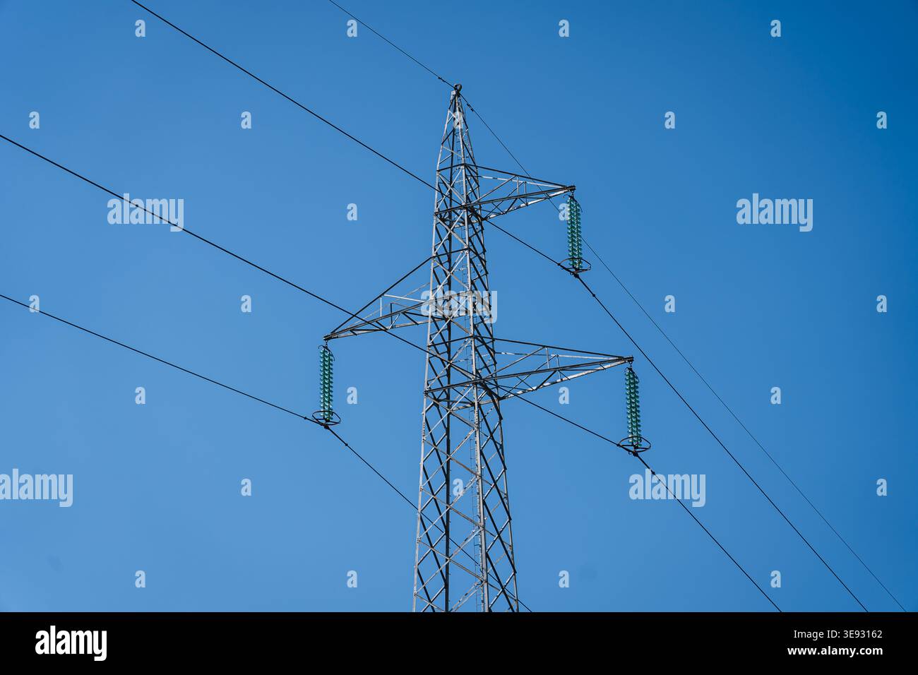 Pylône de transmission debout contre un ciel bleu clair, distribuant l'énergie électrique haute tension via des lignes aériennes pour une utilisation généralisée Banque D'Images