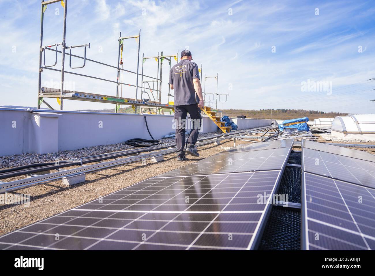 Personne travaillant entre les panneaux solaires sur un toit sous un ciel dégagé, assemblage PV. OBI Baumarkt, Muehlacker, Enzkreis, Allemagne Banque D'Images