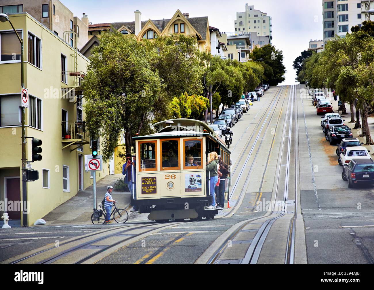 Un téléphérique monte dans une rue escarpée de San Francisco. Les gens regardent depuis les trottoirs les voitures se garer le long de la route. Banque D'Images