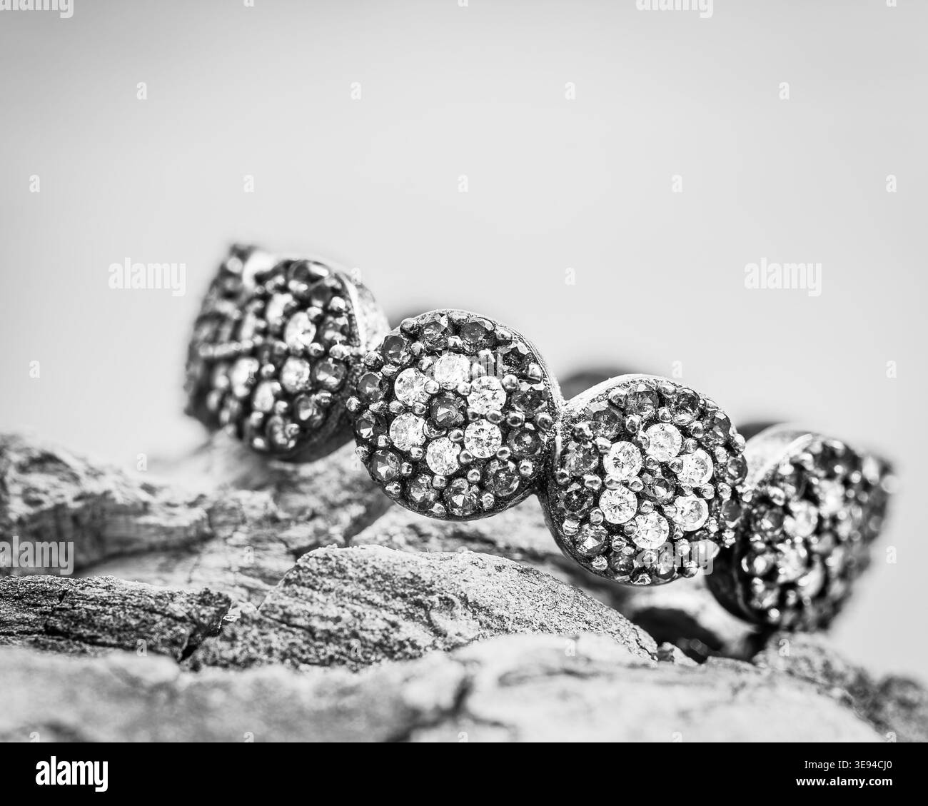 Gros plan noir et blanc d'un anneau en grappe de diamants placé sur une surface rocheuse texturée avec une faible profondeur de champ. Banque D'Images