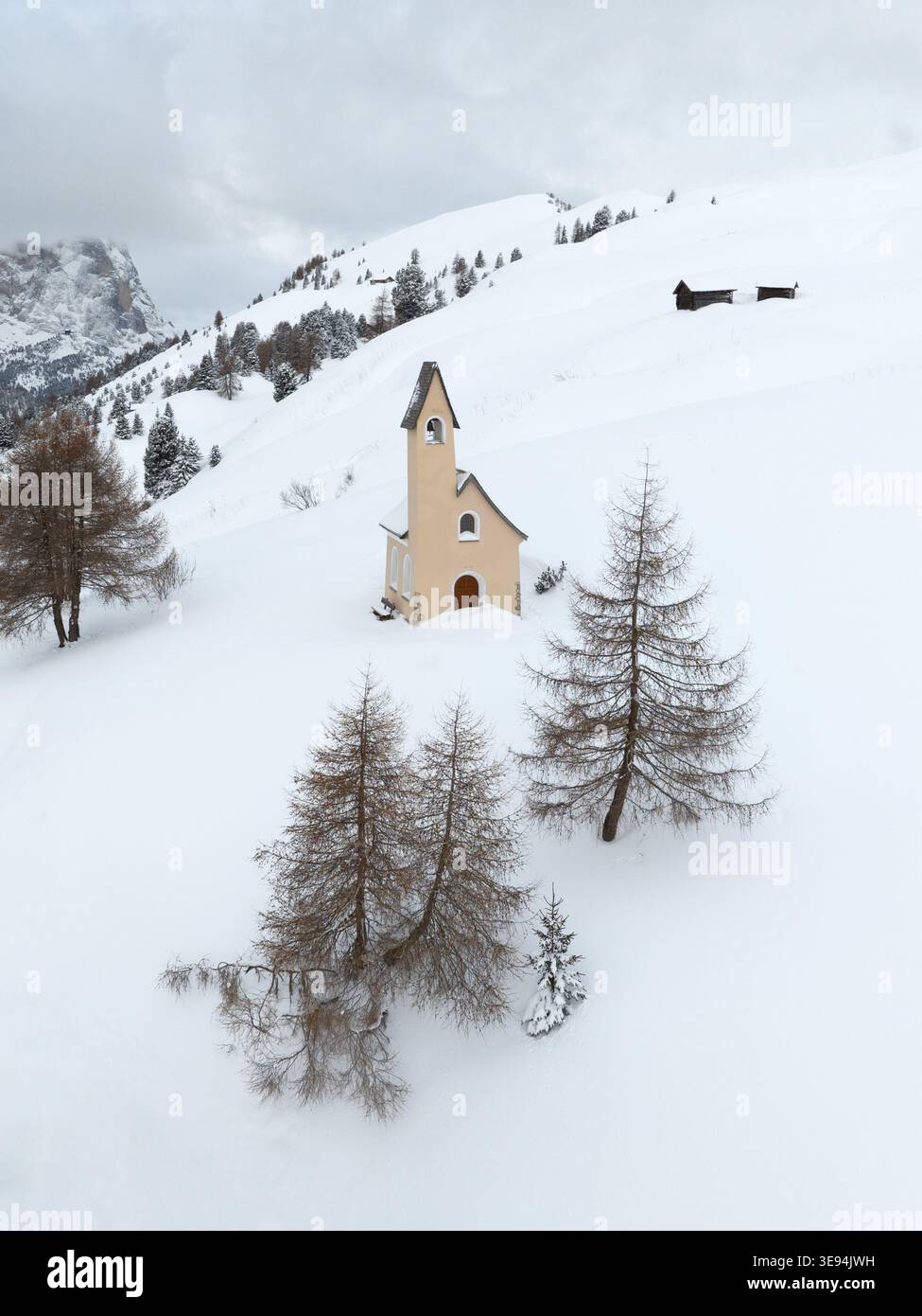 Vue aérienne de Cappella di San Maurizio entourée de pentes enneigées et de pins sous un ciel couvert à Selva di Val Gardena, Trentino-Alto Banque D'Images