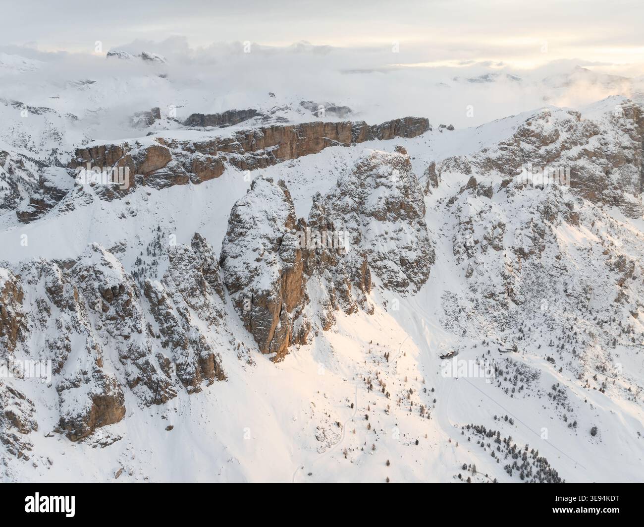Vue aérienne des sommets enneigés et des falaises rocheuses sous un ciel brumeux avec une douce lumière dorée à Selva di Val Gardena, Trentino-Alto Adi Banque D'Images