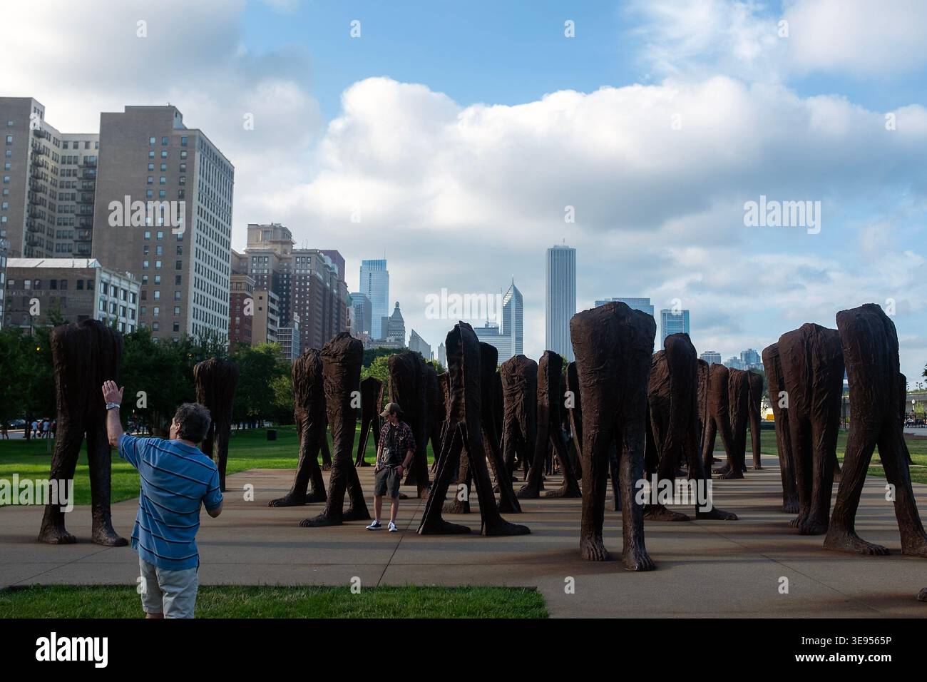 Une personne se tient devant un grand groupe de sculptures en bronze, levant la main comme si elle prenait une photo. Les sculptures sont disposées en rangées à travers un Banque D'Images