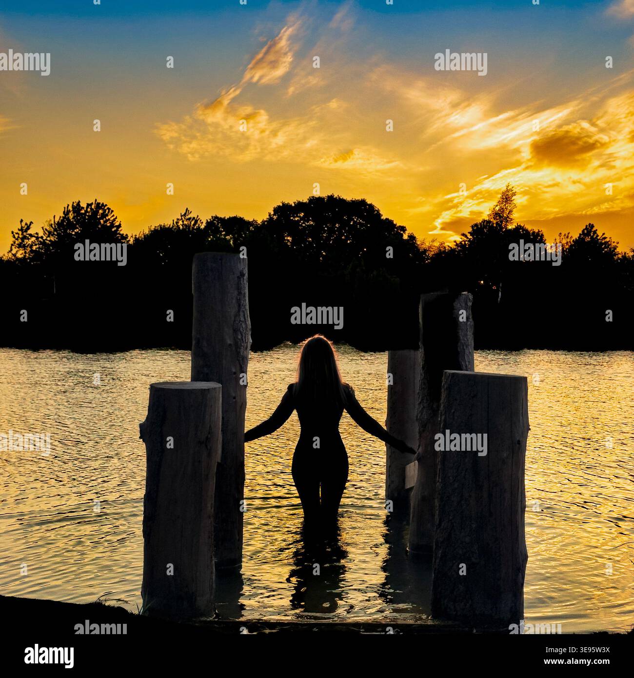 Silhouette d'une femme, partiellement submergée au bord d'un lac de baignade, méditant au lever du soleil. Poolbridge Farm, York. ROYAUME-UNI Banque D'Images