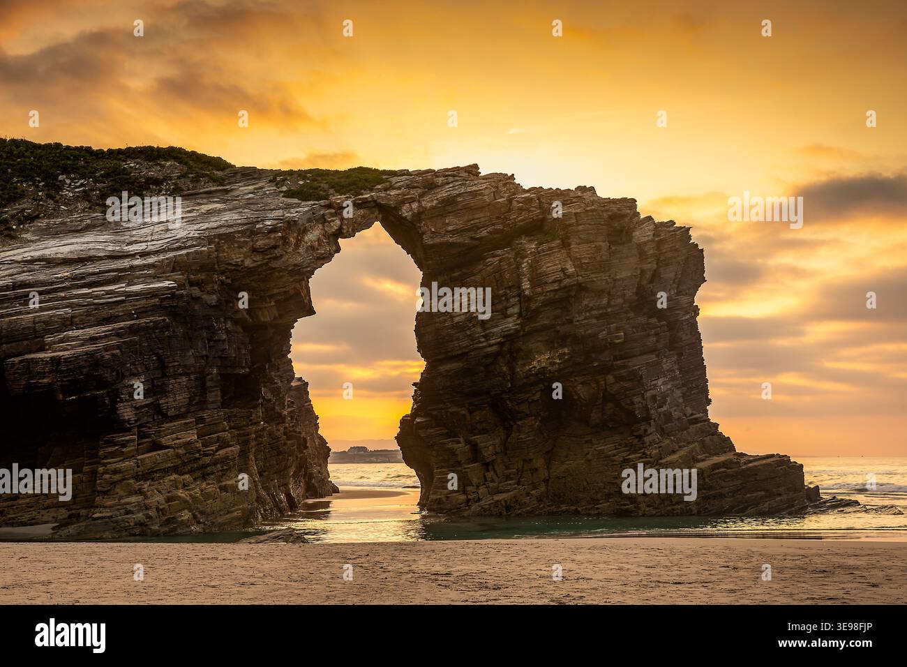 Coucher de soleil à travers Natural Sea Arch sur la plage côtière avec le ciel orange dramatique, Ribadeo, Espagne Banque D'Images
