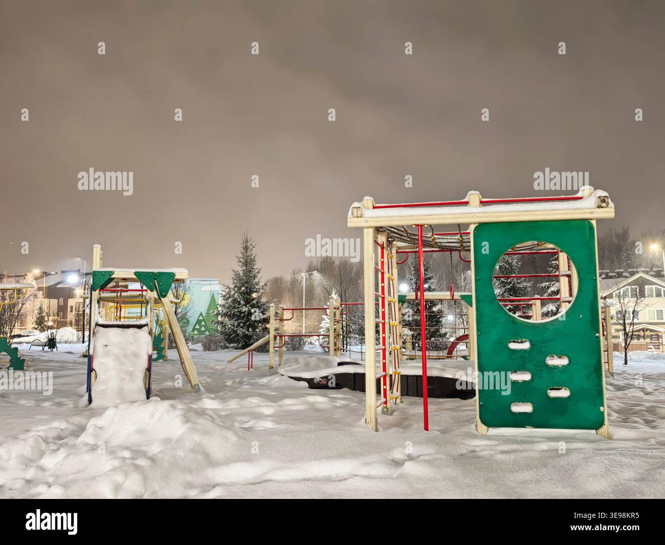 Une aire de jeux est couverte de neige la nuit, avec des structures de jeux visibles dans un parc calme. Banque D'Images