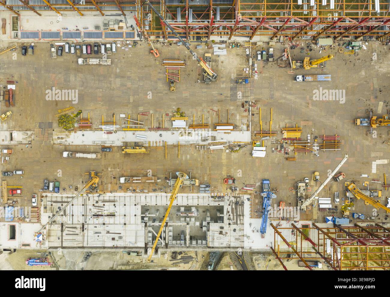 Vue aérienne d'un grand chantier de construction industrielle avec charpentes en acier, grues jaunes et machinerie lourde sur un sol en terre battue à Taiwan. Banque D'Images