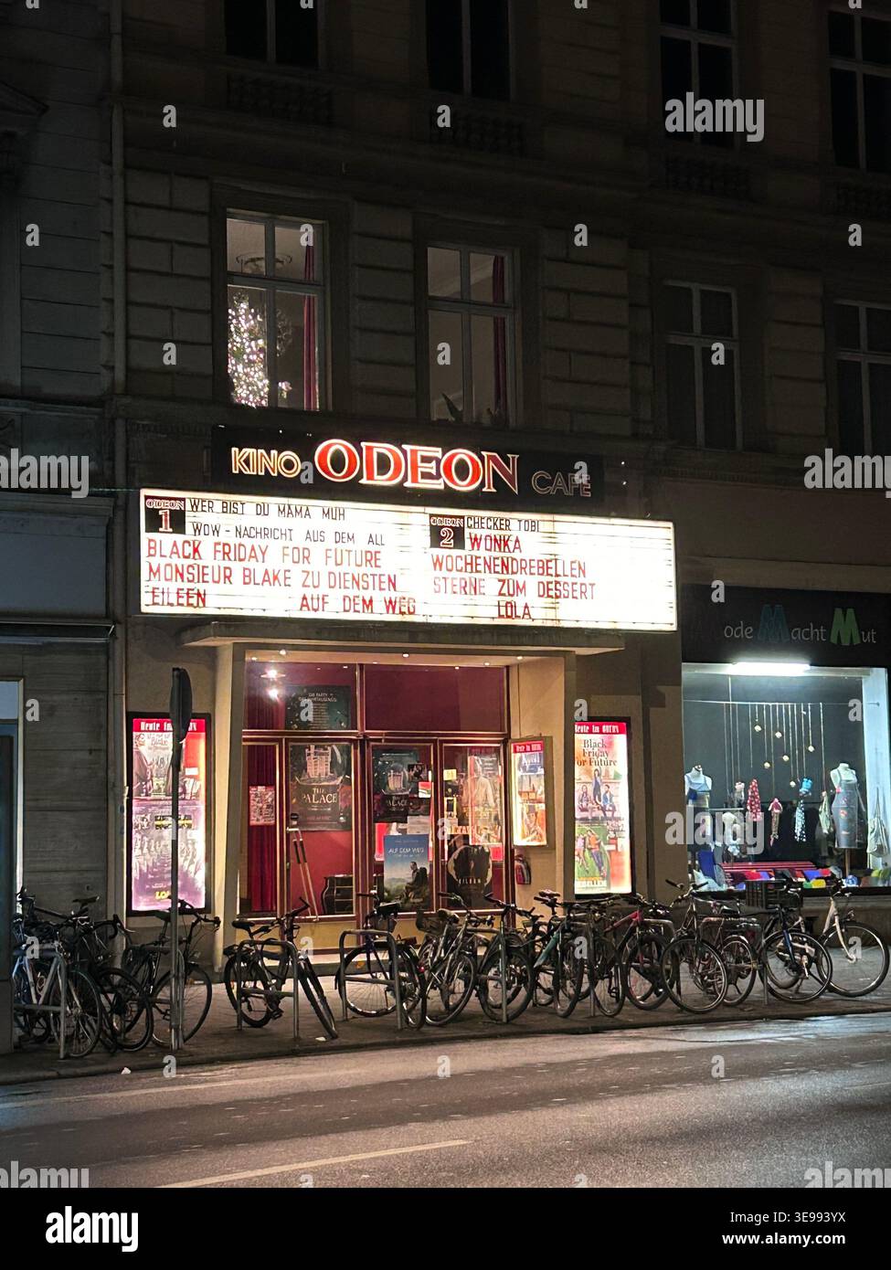 Cinéma historique de l'Odéon à Bamberg, en Allemagne, avec entrée rouge éclairée et vélos garés dehors la nuit. - Image de stock capturée avec un smartphone