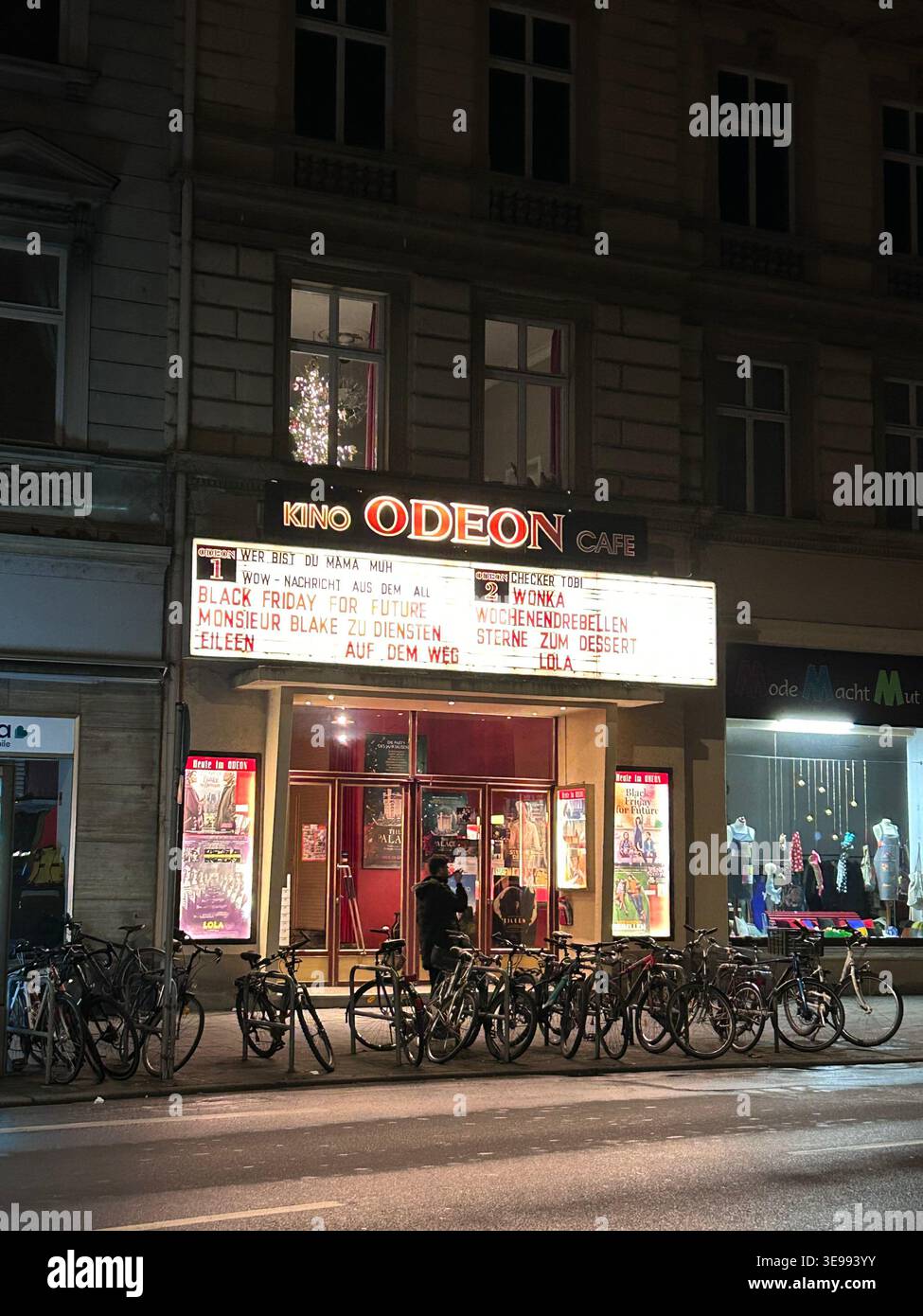 Cinéma historique de l'Odéon à Bamberg, en Allemagne, avec entrée rouge éclairée et vélos garés dehors la nuit. - Image de stock capturée avec un smartphone