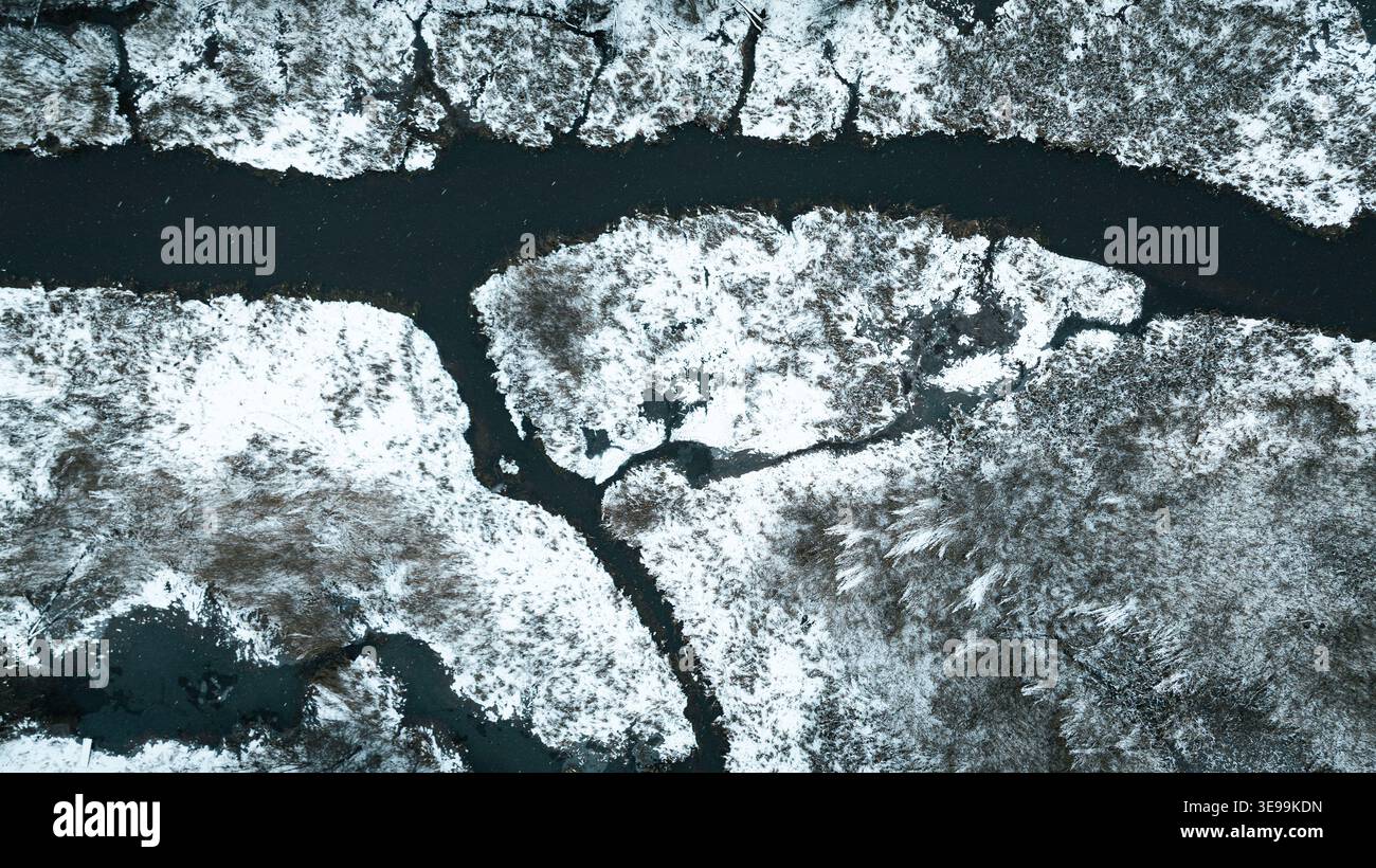 Vue aérienne d'un paysage enneigé avec une rivière sinueuse creusant à travers un pays des merveilles hivernales, avec des arbres enneigés. Banque D'Images