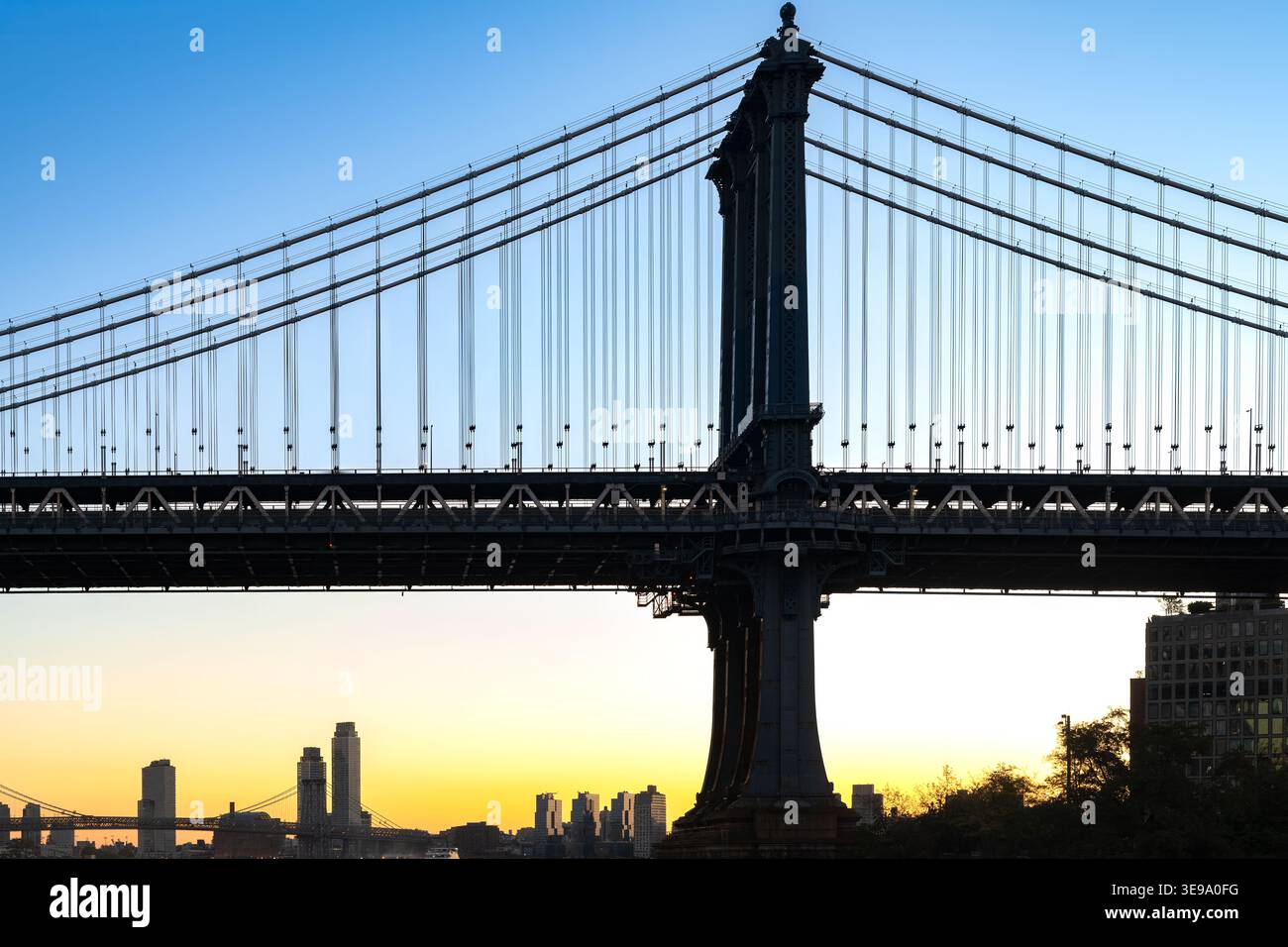 La silhouette du pont de Manhattan se dresse contre la lueur vibrante de l'horizon au petit matin. Banque D'Images