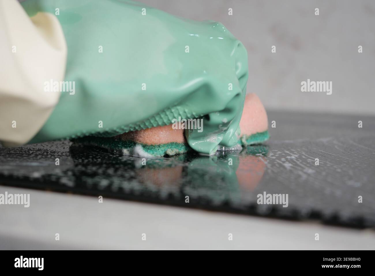 Nettoyer une cuisinière électrique avec une éponge et des gants Banque D'Images