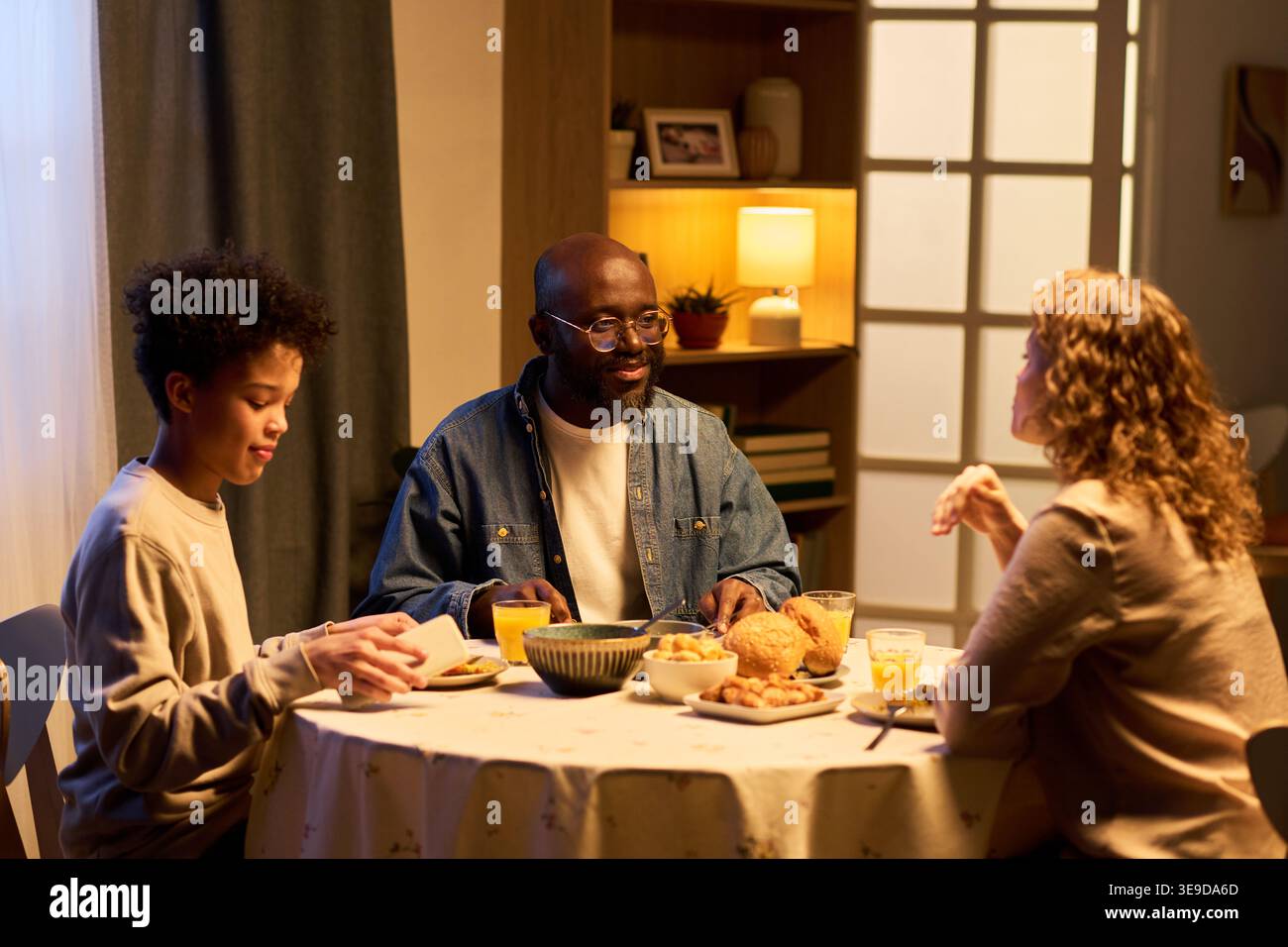 Famille multiethnique partageant le dîner, parlant à la table de la maison et mangeant le repas ensemble, exprimant la connexion et le style de vie quotidien. Utile pour les parents, les liens familiaux Banque D'Images