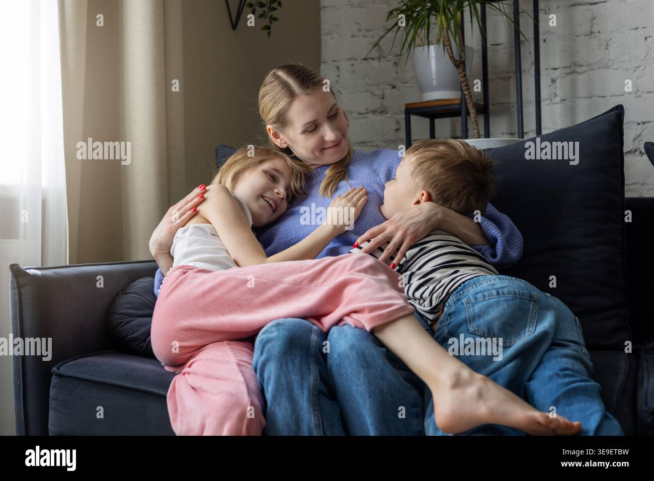 Mère avec deux enfants embrassant sur un canapé confortable à la maison salon. Maman avec adorable fille aimante et fils passant du temps ensemble. Liens familiaux, tr Banque D'Images