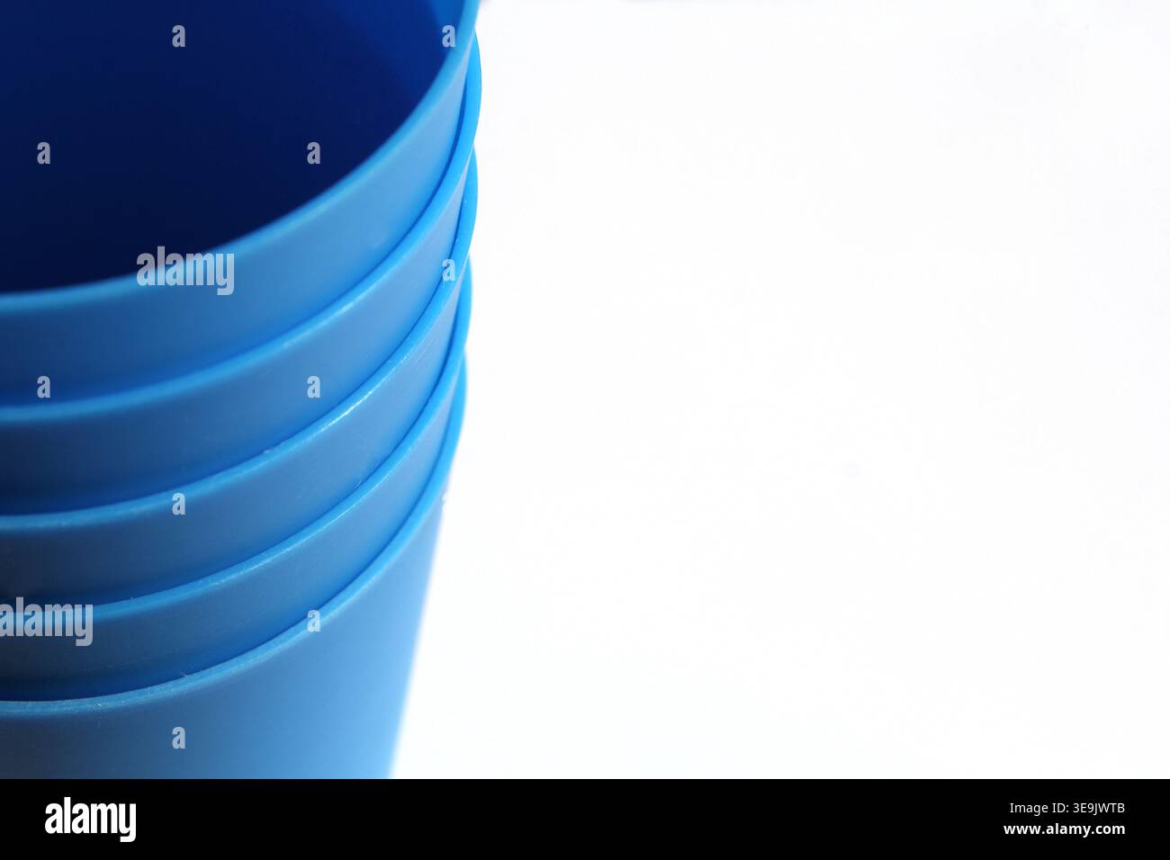 Gros plan d'une pile de gobelets en plastique bleu éclatant sur un fond blanc propre, avec une esthétique minimaliste et moderne Banque D'Images