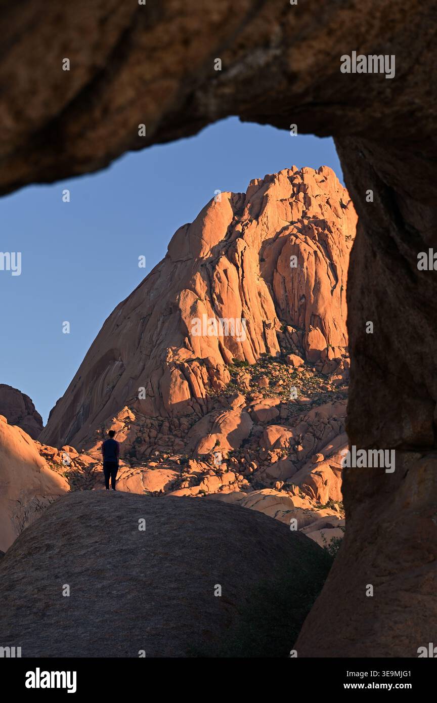 Homme en silhouette et pic de granit illuminé par la lumière du lever du soleil à Spitzkoppe, Namibie Banque D'Images