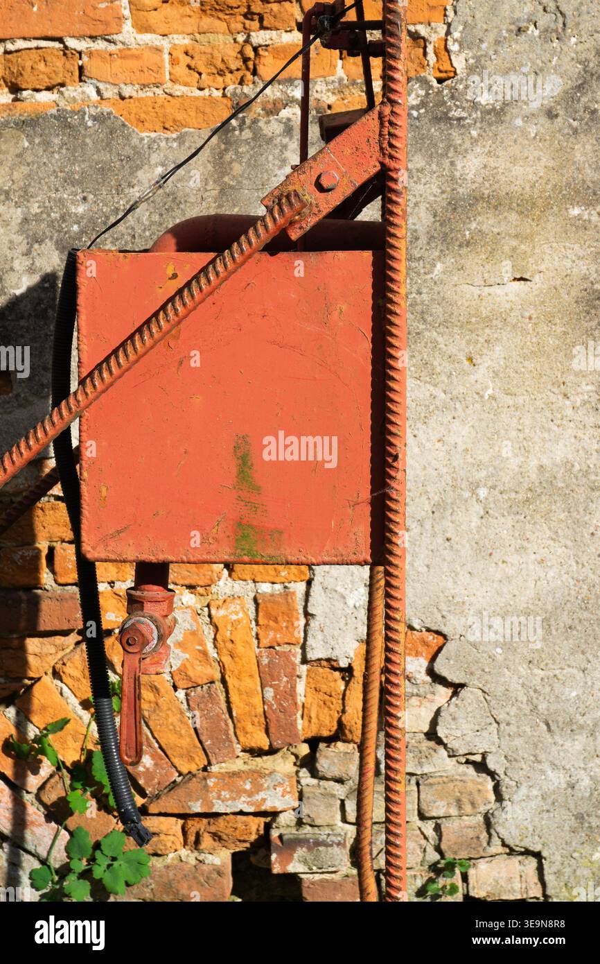Machine inconnue rouge devant le mur de briques avec plâtre qui s'effrite Banque D'Images