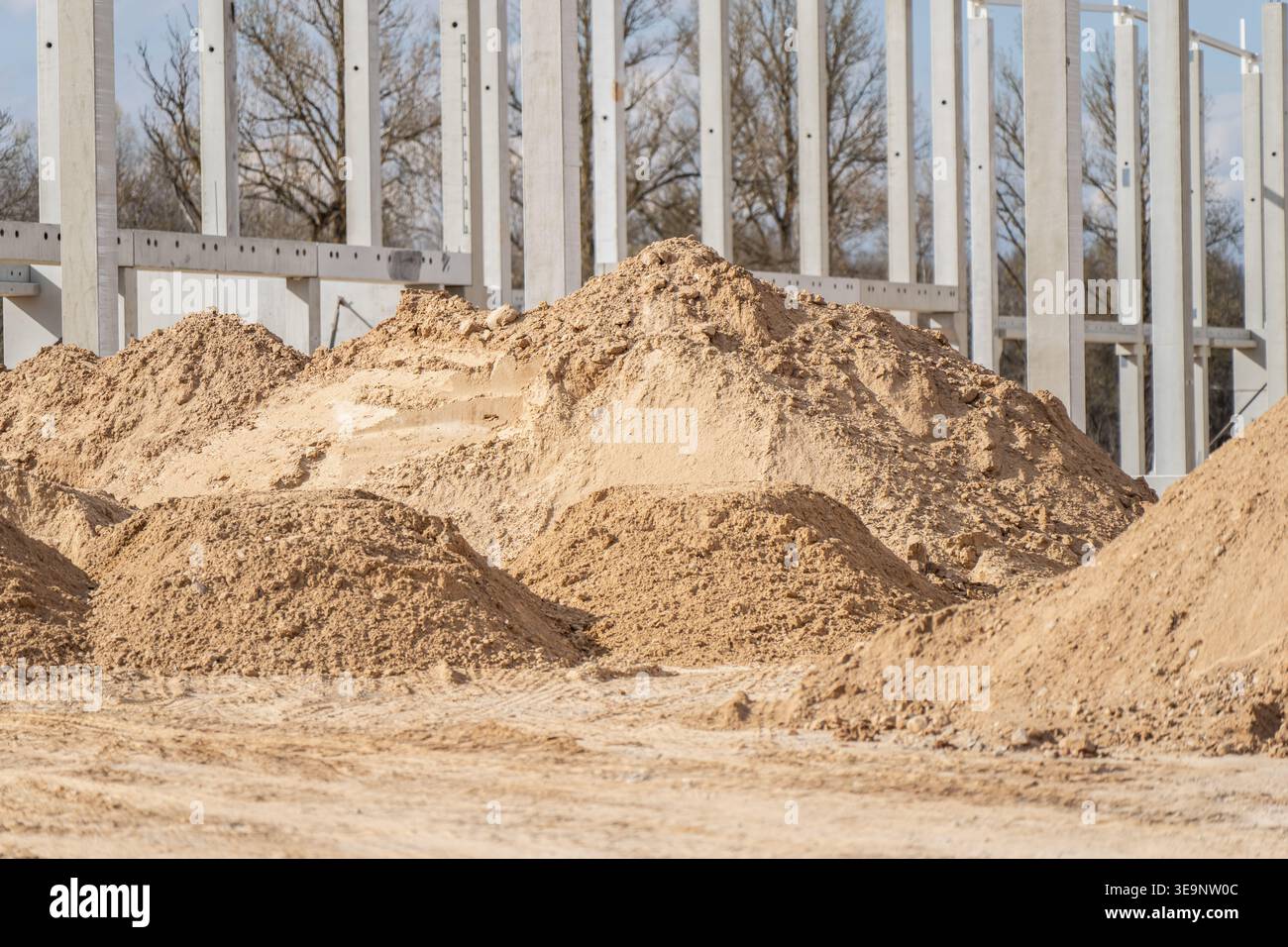 De grands tas de sable et d'agrégats étagés sur le site de construction d'entrepôt à côté de la grille à colonnes en béton pour les travaux de terrassement, le nivellement et l'utilisation de l'approvisionnement en matériaux Banque D'Images