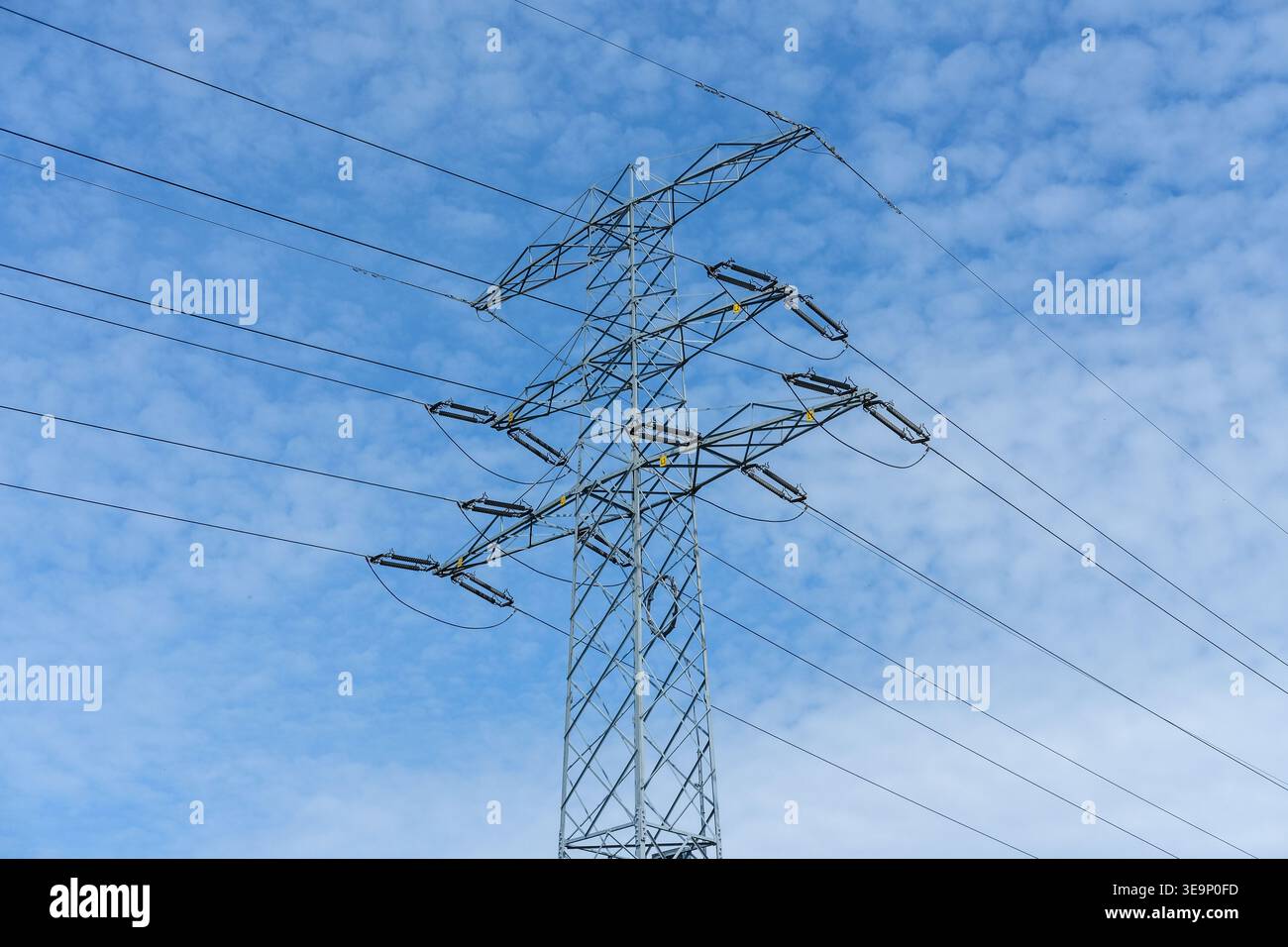 La tour de transmission à haute tension transporte des lignes électriques contre un ciel bleu nuageux dans un environnement extérieur Banque D'Images