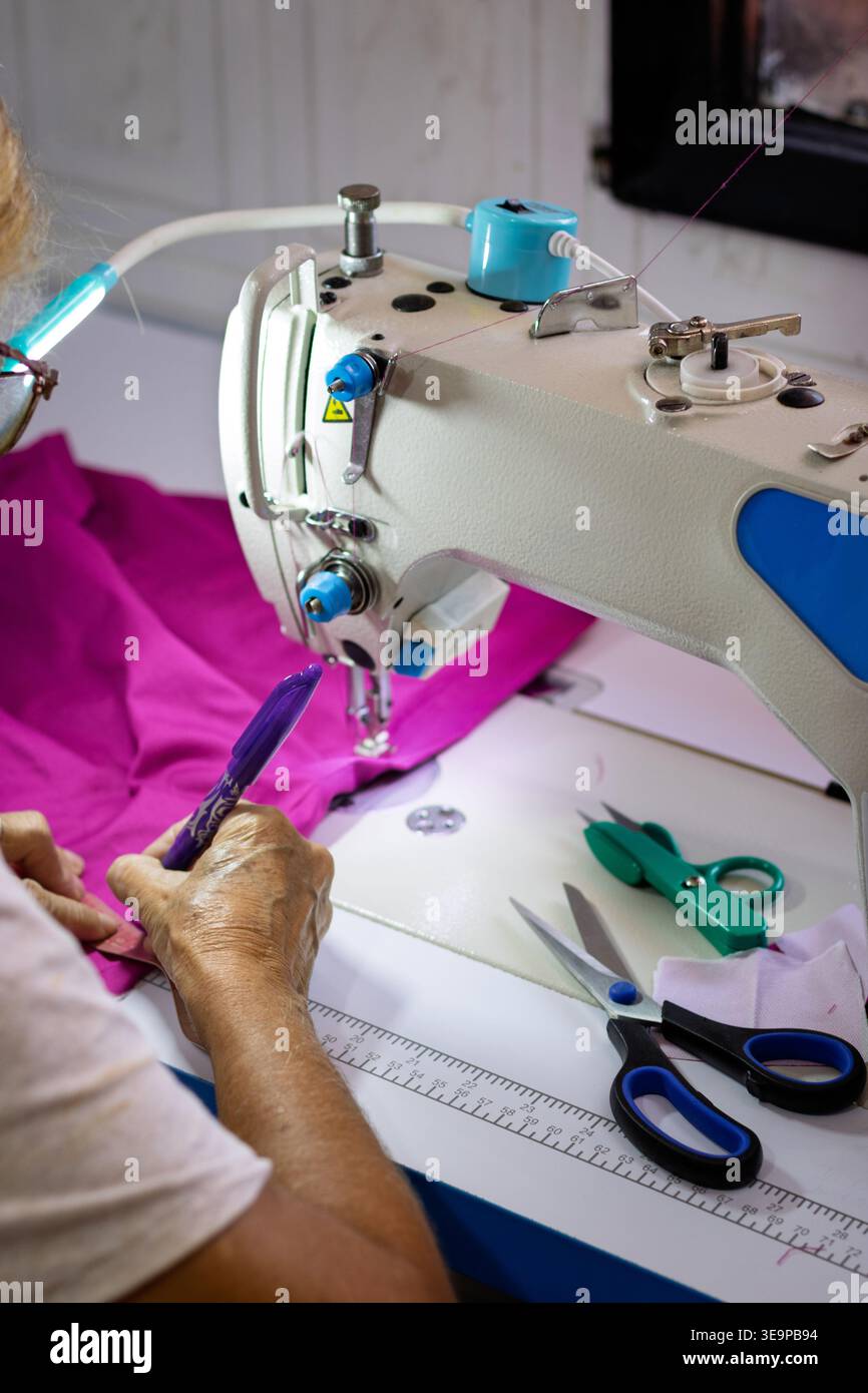 Un homme coud un vêtement avec une machine à coudre. La machine est bleue et blanche Banque D'Images