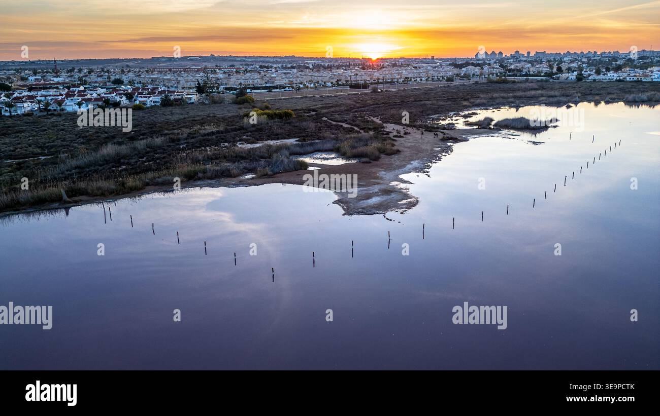 Superbe vue aérienne à l'aube du lac Rose à Torrevieja. Les eaux violettes reflètent le ciel doré, avec des poteaux en bois émergeant de la surface. Dans le Banque D'Images